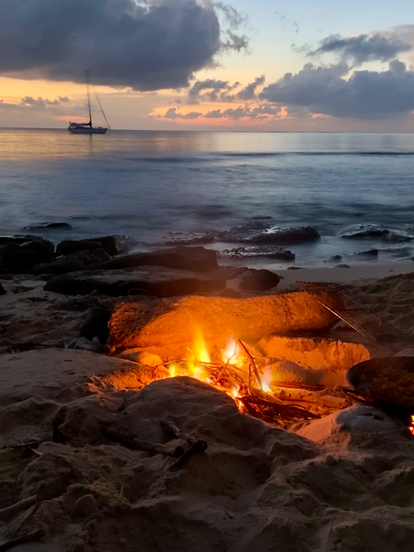 Lagerfeuer am Strand in der Dämmerung, Infinity liegt vor Anker